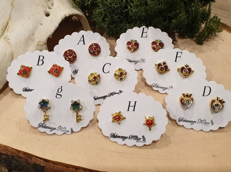 May include: A set of 10 pairs of earrings featuring various designs, including hearts, stars, and keys. Each pair is displayed on a white card with a letter label.