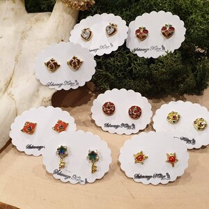 May include: Assortment of gold-tone earrings with colorful enamel and crystal accents. The earrings are displayed on white cards with the text "Always Keep It Magical".