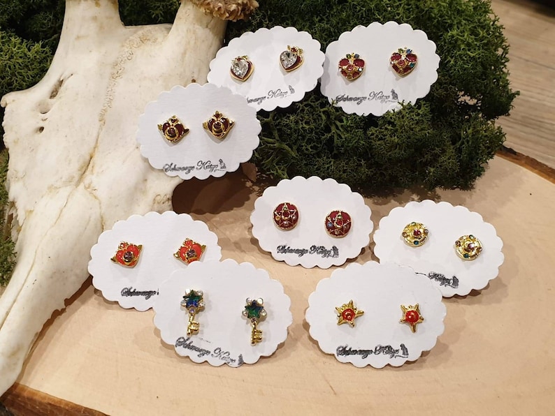 May include: Assortment of gold-tone earrings with colorful enamel and crystal accents. The earrings are displayed on white cards with the text "Always Keep It Magical".