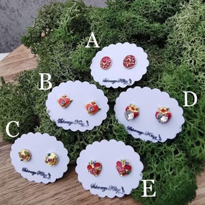 May include: Five pairs of gold-tone earrings with red and multi-colored enamel and rhinestones. The earrings are displayed on white cards with the text "Akagawa Kaguya" on each card.