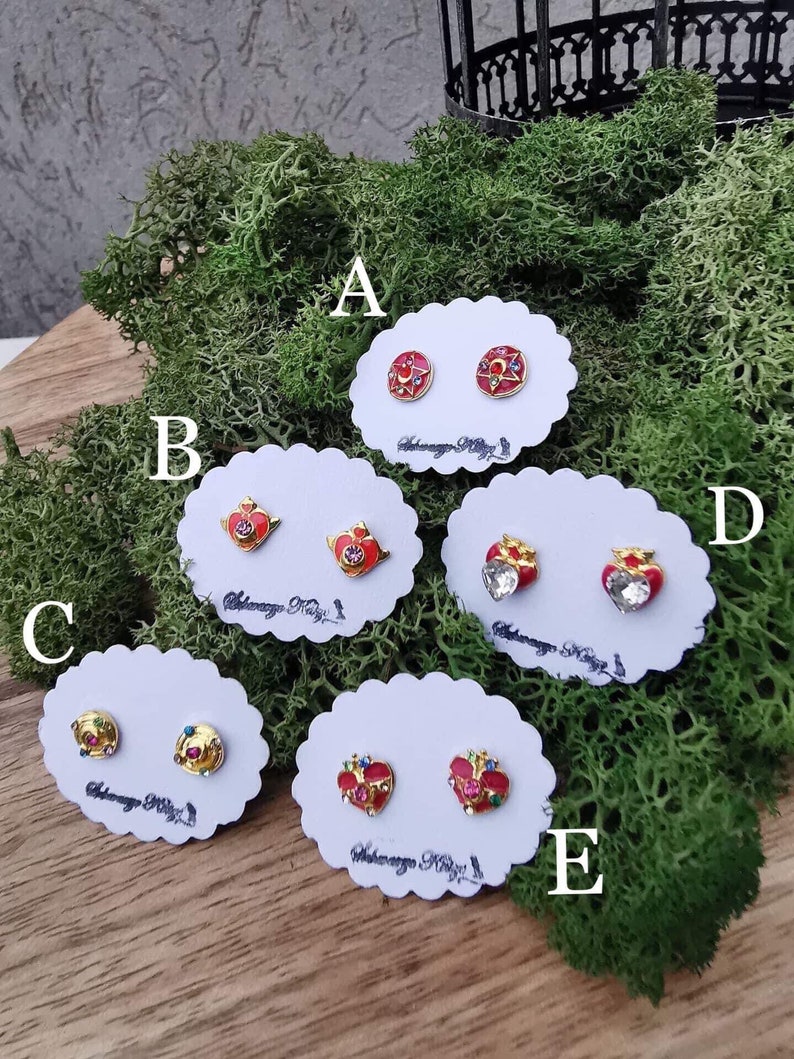 May include: Five pairs of gold-tone earrings with red and multi-colored enamel and rhinestones. The earrings are displayed on white cards with the text "Akagawa Kaguya" on each card.