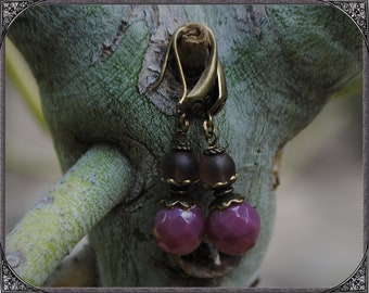 May include: A pair of earrings with a bronze-colored metal design and two purple glass beads on each earring.