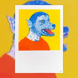 May include: A rectangular art print featuring a stylized illustration of a blue wolf-like creature with a yellow eye and an open mouth showing teeth and a red tongue. The creature wears an orange shirt against a bright yellow background.