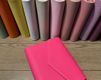 Op de afbeelding: Een collectie van getextureerde mappen in envelopstijl in diverse kleuren, waaronder oranje, geel, wit, beige, lichtroze, oudroze, mauve en lavendel, met een felroze map die prominent op de voorgrond is geplaatst.