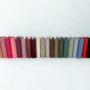 May include: A collection of colorful, vertical wallets in various shades, including pink, red, brown, green, and blue. The wallets are arranged in a row, showcasing a range of hues and textures. The wallets are standing upright.