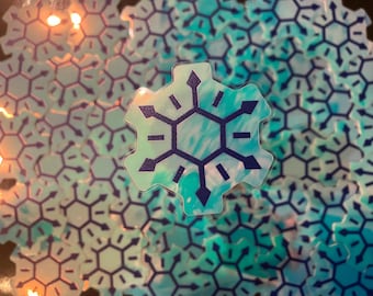 Pode incluir: Um close-up de um adesivo de floco de neve azul e branco com um design hexagonal. O adesivo é cercado por outros adesivos de floco de neve.