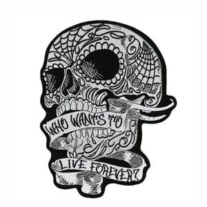 May include: A black and white embroidered patch featuring a stylized skull with intricate line work and spiderweb patterns. A banner draped across the jaw area contains the text "WHO WANTS TO LIVE FOREVER?" in a bold, dark, hand-lettered font.
