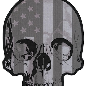 Pode incluir: Um patch de caveira em tons de cinza com um design de bandeira americana. As características da caveira são detalhadas, com as estrelas e listras da bandeira integradas. O patch tem uma borda preta.
