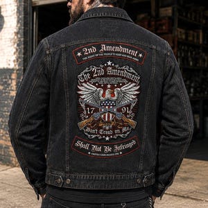 May include: A black denim jacket featuring a large back patch with a graphic of an eagle, two crossed rifles, and the text 2nd Amendment, 1791, Don't Tread on Me, and Shall Not Be Infringed. The jacket has a classic collar and button-down front.