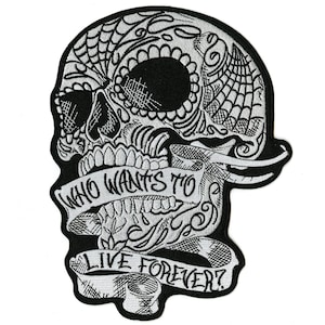 Pode incluir: Patch bordado em preto e branco em forma de caveira de açúcar. A caveira apresenta intrincados desenhos florais e semelhantes a teias. Uma faixa na caveira diz "WHO WANTS TO LIVE FOREVER?"