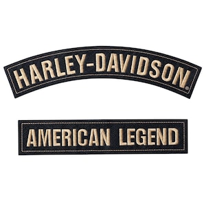 Könnte beinhalten: Zwei schwarze, gestickte Aufnäher. Der obere Aufnäher ist bogenförmig und trägt in beigefarbenem Garn die Aufschrift "HARLEY-DAVIDSON". Der untere Aufnäher ist rechteckig und trägt in beigefarbenem Garn die Aufschrift "AMERICAN LEGEND". Beide Aufnäher haben einen gestickten Rand.