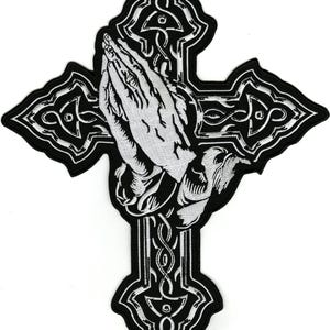 Peut inclure: Écusson brodé noir et blanc représentant une croix avec des mains jointes en prière au centre. La croix présente des détails ornés et un fond pointu. Les mains sont en position de prière, avec des ombres détaillées.