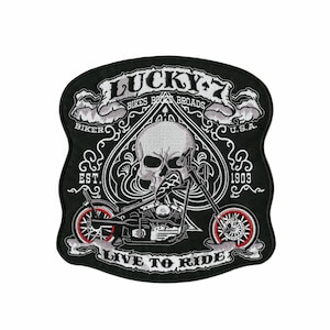 May include: Black embroidered patch with a skull, motorcycle, and the text "LUCKY 7 BIKES BOOZE BROADS LIVE TO RIDE". The patch has a spade shape with red and white accents and the text "U.S.A. 1903".