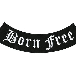 May include: Black, curved patch with the words "Born Free" embroidered in white, gothic-style lettering. The patch has a rectangular shape with angled corners, suitable for sewing onto clothing or accessories.