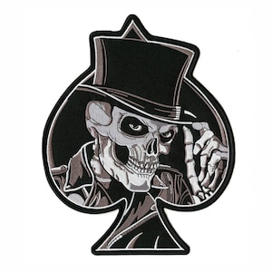May include: A black and white patch featuring a skull wearing a top hat and a jacket, set against a black spade shape. The skull has a stern expression, with a finger pointing forward. The patch is likely for clothing or accessories.