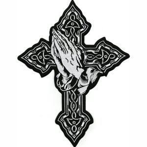 May include: A black and white embroidered patch featuring a detailed illustration of two hands pressed together in prayer, positioned over a decorative cross with intricate line work and a solid black border outline.
