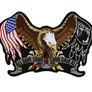Pode incluir: Patch bordado com uma águia com as asas abertas, a bandeira americana e um emblema POW-MIA. O texto "ALL GAVE SOME, SOME GAVE ALL" está em uma faixa. O patch tem uma borda preta.