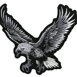 May include: Embroidered patch featuring a detailed bald eagle in flight. The eagle is depicted with its wings fully spread, showcasing intricate feather details in shades of gray and white against a black background. The patch is designed with a black border.