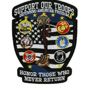 Pode incluir: Patch bordado com o texto "SUPPORT OUR TROOPS DEFENDING AMERICAN FREEDOM" e "HONOR THOSE WHO NEVER RETURN". Apresenta uma cruz com um capacete, botas e um rifle, juntamente com insígnias dos ramos militares e um desenho da bandeira americana.