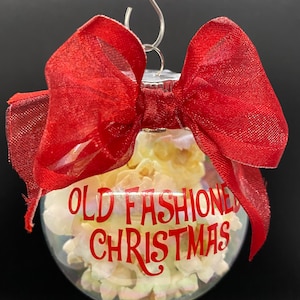 May include: A clear glass Christmas ornament with a red bow and the text "OLD FASHIONED CHRISTMAS" in red lettering. The ornament is filled with white popcorn.