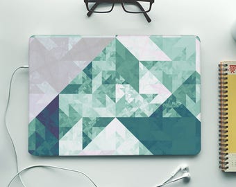 Könnte beinhalten: Ein Laptop mit einem geometrischen Muster auf dem Deckel. Das Muster besteht aus Dreiecken in Grün-, Blau- und Weißtönen. Der Laptop befindet sich auf einer weißen Oberfläche mit einer Brille, einem Notizbuch und einer Tasse Kaffee.