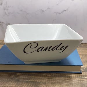 May include: White ceramic bowl with the word "Candy" written in black cursive lettering.