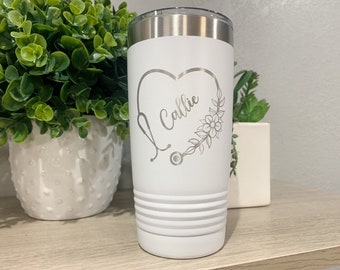 May include: White stainless steel tumbler with a silver engraved design of a stethoscope inside a heart with the name "Callie" and floral accents.