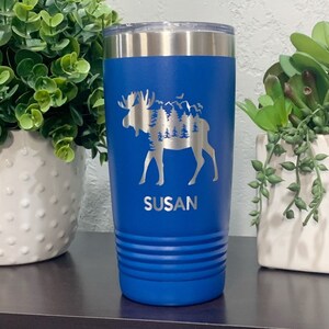 May include: A blue stainless steel tumbler with a moose silhouette design and the name "SUSAN" engraved on the front.