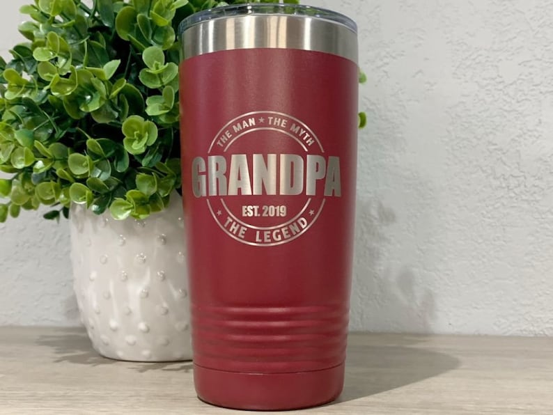May include: A red stainless steel tumbler with a silver inscription that reads "The Man * The Myth * Grandpa * Est. 2019 * The Legend".