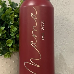 May include: A red stainless steel water bottle with a black lid and a silver inscription that reads "Mama est. 2021".