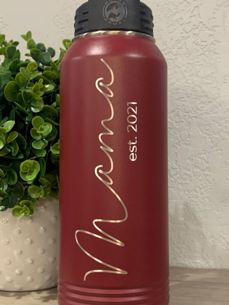 May include: A red stainless steel water bottle with a black lid and a silver inscription that reads "Mama est. 2021".
