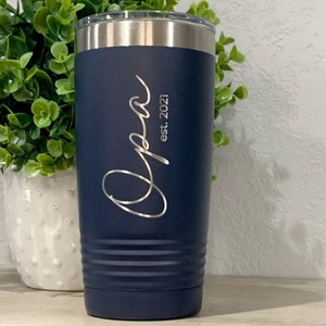May include: A navy blue stainless steel tumbler with a silver lid. The tumbler has the word "Opa" engraved on it, along with the text "est. 2021".