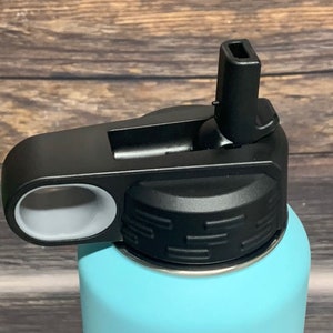 May include: Close-up of a black and gray water bottle lid with a flip-top spout. The lid has a gray ring around the spout and a textured black top.