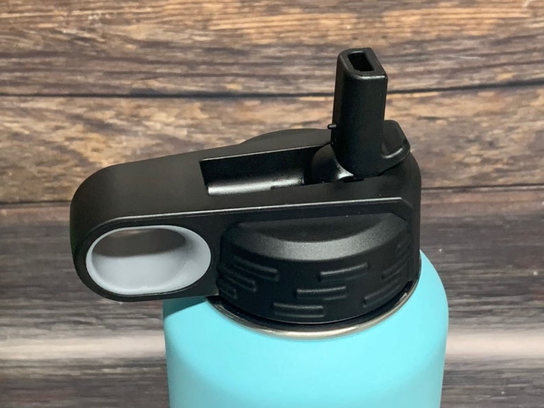 May include: Close-up of a black and gray water bottle lid with a flip-top spout. The lid has a gray ring around the spout and a textured black top.