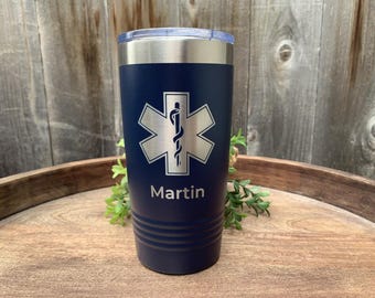 May include: A blue stainless steel tumbler with a silver medical symbol and the name "Martin" engraved on it.