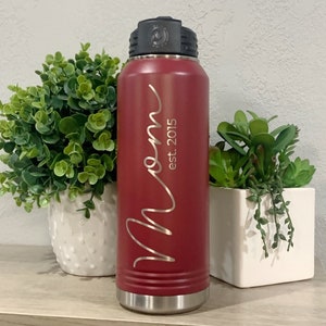 May include: A red stainless steel water bottle with a black lid and a silver base. The bottle has the word "Mom" written in cursive with "est. 2015" underneath.