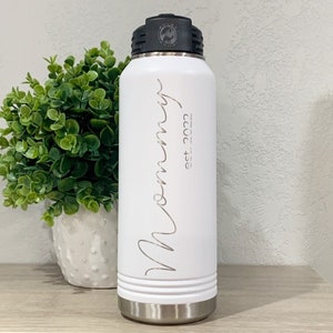 May include: White stainless steel water bottle with a black lid and a white inscription that reads "Mommy est. 2022".