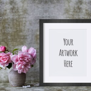 May include: A black picture frame with a white mat and the text "YOUR ARTWORK HERE" inside the frame. A vase with pink flowers sits in front of the frame.