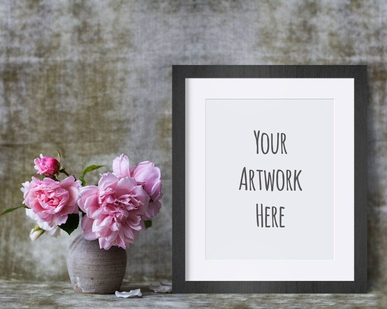 May include: A black picture frame with a white mat and the text "YOUR ARTWORK HERE" inside the frame. A vase with pink flowers sits in front of the frame.