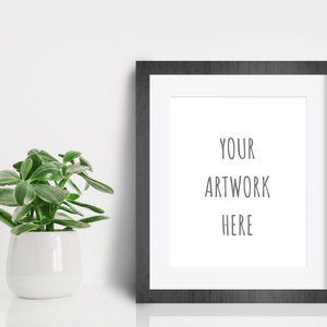 May include: A black picture frame with a white mat and the text "YOUR ARTWORK HERE" inside. A small green plant in a white pot is to the left of the frame.