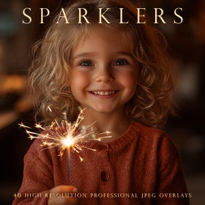 May include: A young girl with blonde curly hair smiles while holding a lit sparkler. The sparkler is a bright yellow and orange color and is creating a lot of sparks. The girl is wearing a brown sweater.