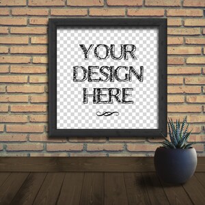 May include: A black framed picture with a white background and the text "YOUR DESIGN HERE" in black. The picture is hanging on a brick wall with a small green plant in a black pot in the foreground.