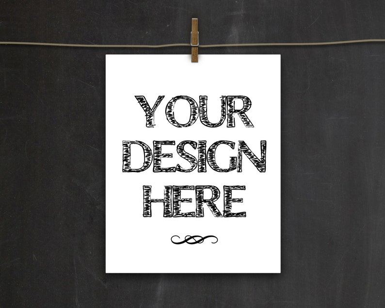 以下が含まれることがあります： 白い紙に黒い手書きの文字で「YOUR DESIGN HERE」と書かれている。紙は木製の洗濯ばさみで洗濯ロープにかけられている。