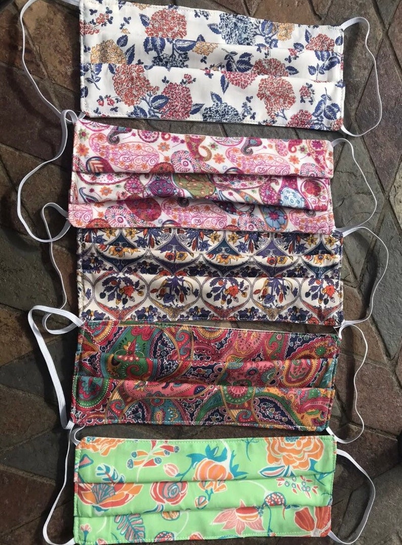 May include: Five different patterned face masks with white elastic ear loops. The masks are made of fabric and have a pleated design. The patterns include floral, paisley, and geometric designs.