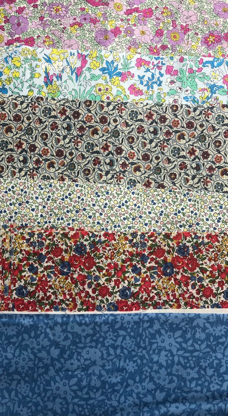 May include: A collection of six fabric swatches featuring various floral designs. The swatches are stacked vertically, starting with a pink and white floral pattern, followed by a blue and white floral pattern, a brown and white geometric pattern, a white and yellow floral pattern, a red and white floral pattern, and finally a blue and white floral pattern.