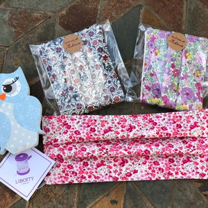 May include: A pink and white floral fabric face mask with a light purple elastic band. The mask is handmade and packaged with a small tag that says "Handmade with Love". Two additional pieces of fabric are also included, one with a blue and white floral pattern and one with a purple and white floral pattern.