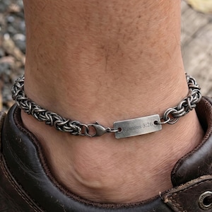 May include: A silver anklet with a chain design. It features a rectangular tag inscribed with "Romans 3:26". The anklet is worn on an ankle above a brown leather shoe.