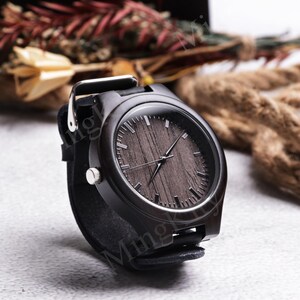 K&ouml;nnte beinhalten: Eine schwarze Holzarmbanduhr mit dunklem Holzmaserungszifferblatt und schwarzem Lederarmband. Die Uhr hat silberfarbene Akzente und eine klassische analoge Anzeige. Ein stilvolles Accessoire.