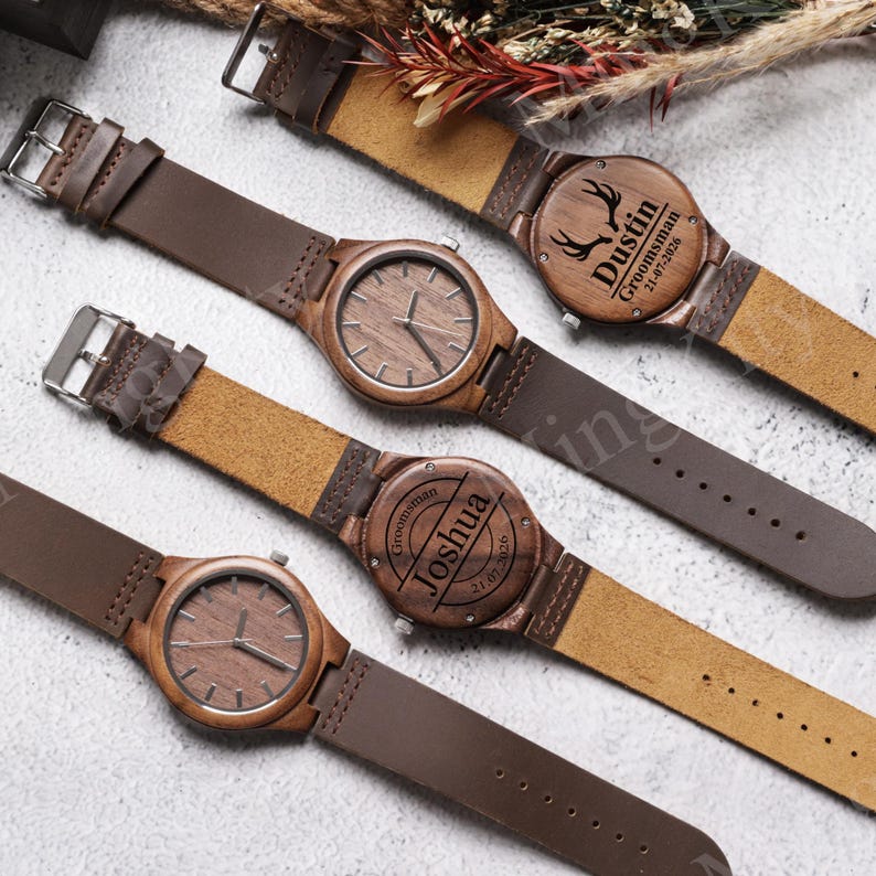 K&ouml;nnte beinhalten: Vier Holzuhren mit braunen Lederarmb&auml;ndern. Die Zifferbl&auml;tter der Uhren sind holzfarben mit einfachen Zeigern. Zwei Uhren haben personalisierte Gravuren auf der R&uuml;ckseite, einschlie&szlig;lich Namen und Daten. Die Uhren liegen auf einer hellen Oberfl&auml;che.
