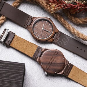 K&ouml;nnte beinhalten: Zwei Holzuhren mit braunen Lederarmb&auml;ndern. Die Zifferbl&auml;tter der Uhren sind dunkelbraun mit silbernen Zeigern und Markierungen. Auf einer Uhr steht der Text "Thank you for always be my side, I'll love you till the end of time. Lora".